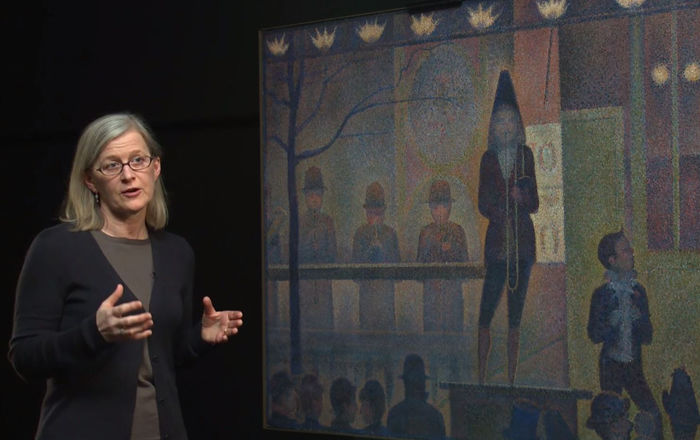 A woman stands before a monumental painting by Georges Seurat