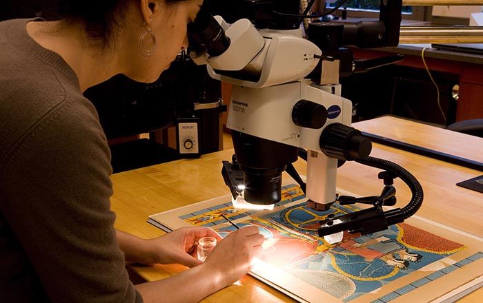 A woman looking through a telescope, examining a colorful work of art on paper