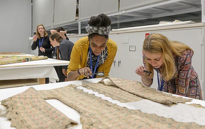 Two young women use magnifying glasses to inspect a textile.